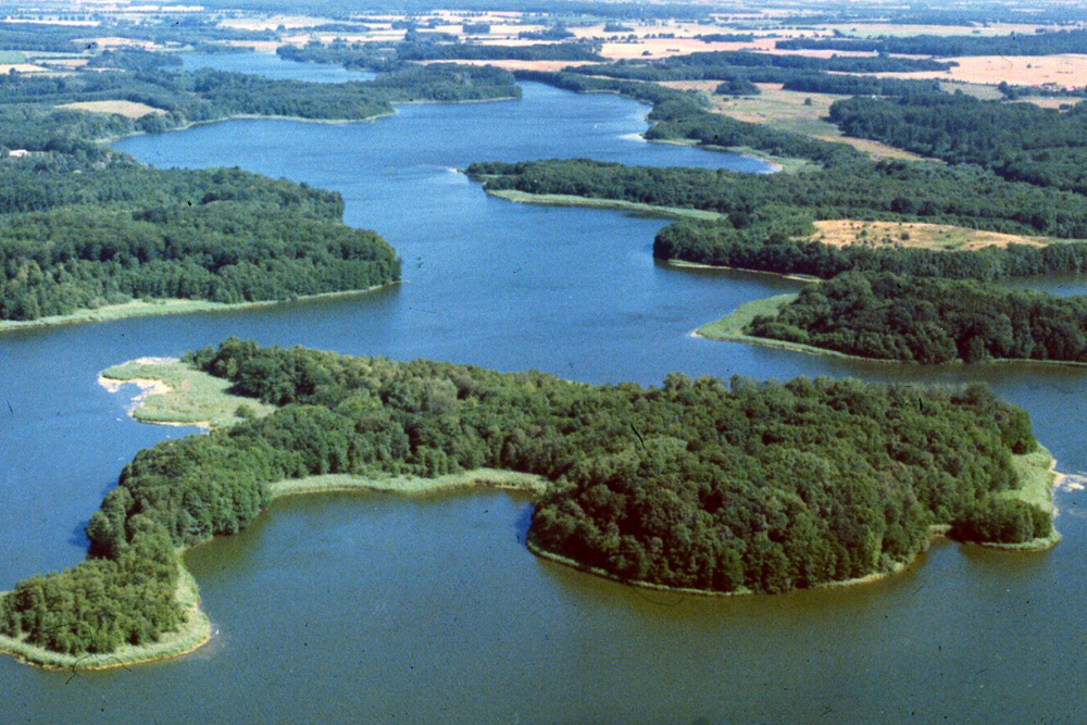 Die Schaalsee-Landschaft aus der Luft betrachtet. Man sieht den See, eine große Insel und die Umgebung mit Wäldern und Feldern.